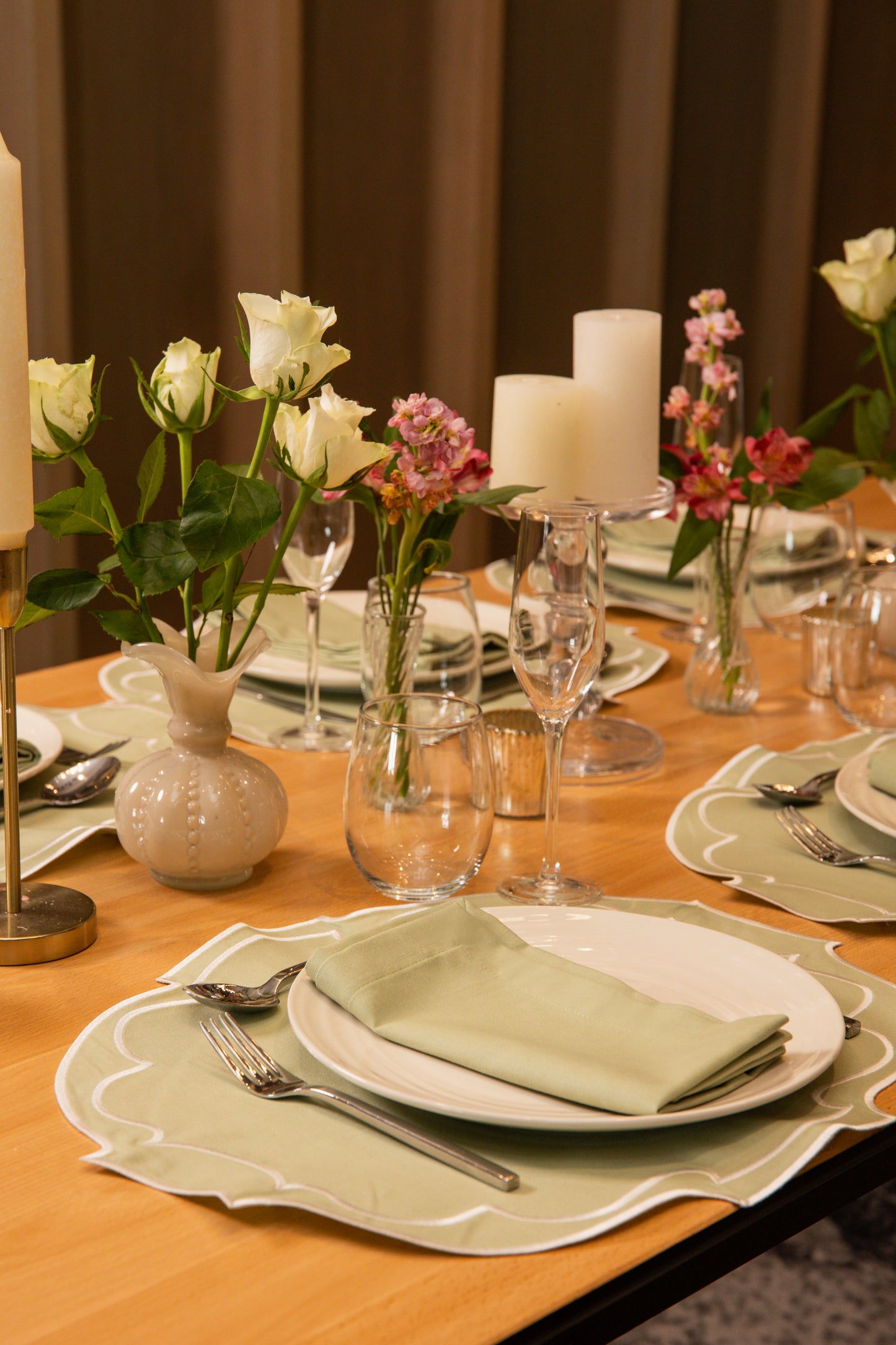 Top Tables Taylor Placemat & Napkin in Sage Green cotton, with embroidered trim, styled on a refined table with florals and candles.
